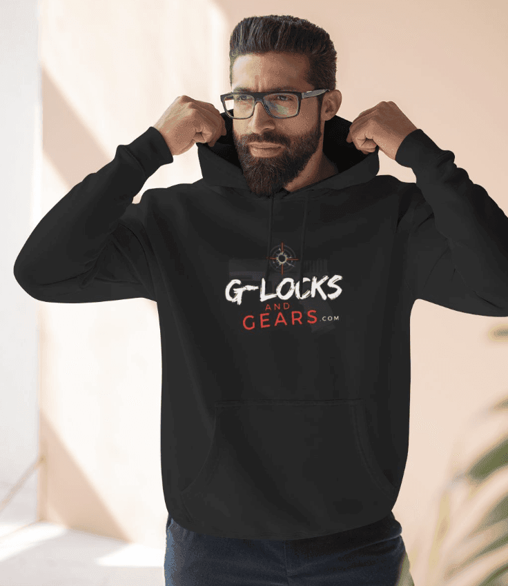 Person in glasses and beard adjusting black hoodie with branded text, standing in sunlit room.